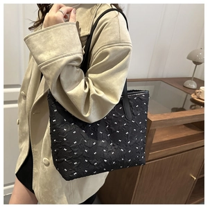 Détail du sac cabas en jacquard noir avec nœuds blancs sur un manteau en daim beige