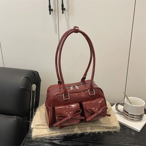 Dark red patent leather ballet style bag with bows and silver zippers on beige fabric