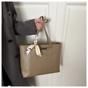 Close-up of khaki tote bag with metal bar detail and decorative floral silk scarf