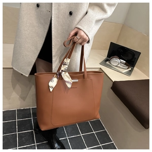 Detail of brown leather tote bag featuring a front pocket and decorative printed silk scarf