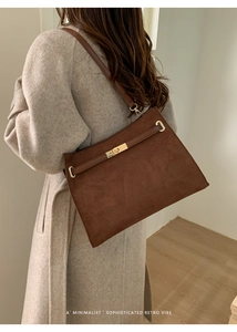 Détail d'un sac cabas en daim marron avec boucle dorée et bandoulière en cuir sur modèle