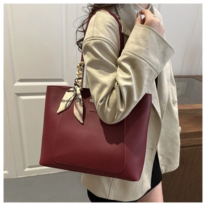 Shoulder shot of a burgundy leather tote bag with a decorative scarf on a model
