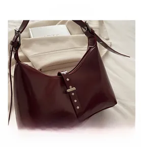 Dettaglio ravvicinato della borsa in pelle bordeaux con fibbia decorativa e rivetti metallici