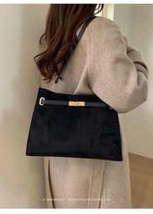 Détail d'un sac cabas en daim noir avec fermoir doré porté sur un manteau en laine