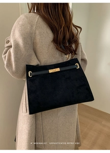 Détail du sac cabas en daim noir avec fermoir en métal doré sur un manteau beige