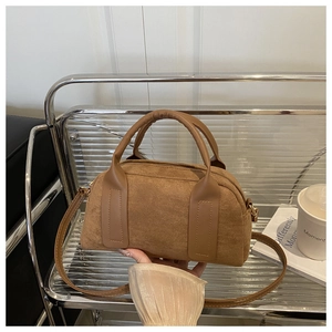Detail einer braunen Boston-Tasche aus Wildleder mit glatten Ledergriffen und Goldteilen