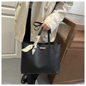 Close-up of black tote bag with silver metal bar and printed silk scarf on handle