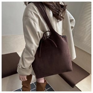 Detail of dark brown suede tote bag featuring a decorative bow knot on the shoulder strap