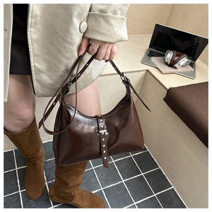 Dettaglio di una borsa in vernice marrone scuro con borchie e tracolla regolabile con fibbia