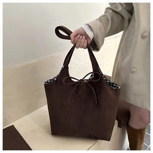 Detail of brown suede tote bag with bow tie closure and classic plaid lining interior