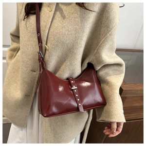 Dettaglio della borsa croissant in pelle verniciata bordeaux con cappotto beige