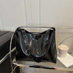 Grande borsa tote nera lucida con tracolla ad occhielli in un ambiente urbano moderno