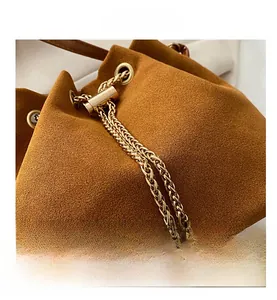 Detail of brown suede bucket bag featuring golden chain drawstring and large pearl pendants