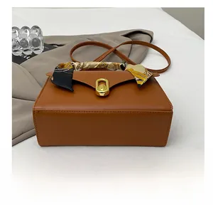 Detail of a brown leather handbag featuring a silk scarf handle and golden oval lock
