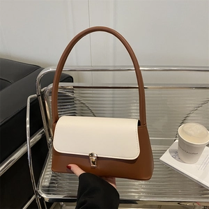 Modern brown and white contrast underarm bag with gold metal buckle on a minimalist shelf
