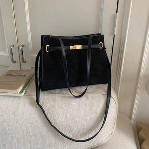 Sac cabas minimaliste en daim noir avec boucles dorées posé sur un canapé blanc
