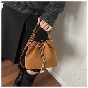 Detail of brown suede bucket bag featuring golden chain drawstring and white pearl charms