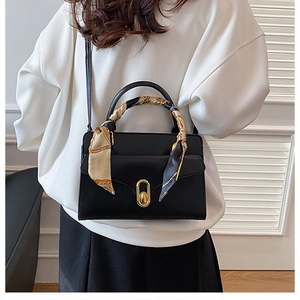 Detail of black handbag with golden oval twist lock and floral silk scarf wrapped on handle