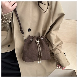 Detail view of dark coffee suede bucket bag with gold chain and pearl tassel accents