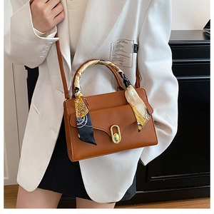 Detail of a brown leather crossbody bag with golden buckle and silk scarf handle