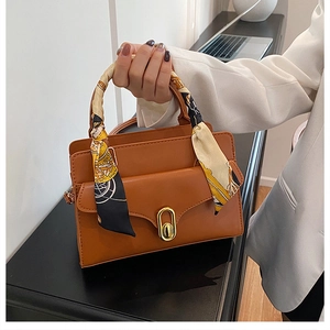 Close-up of brown leather handbag featuring gold twist lock and printed silk scarf handle