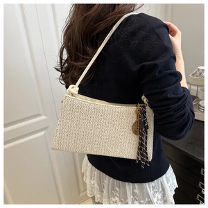 Primer plano de bolso tejido crema con amuleto de llave decorativo y borla de flecos