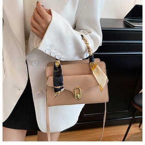 Close-up of a square handbag featuring a patterned silk scarf handle and golden twist lock