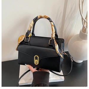 Detail of black trapezoid handbag with a floral silk scarf handle and golden twist lock