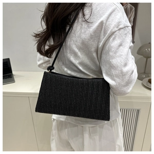Close-up of black woven underarm bag with knot detail on slim strap in lifestyle setting