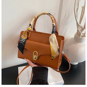 Close-up of caramel leather handbag with silk scarf handle and gold buckle detail