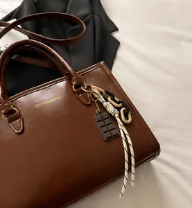 Detail of dark brown leather tote bag with gold lettering and decorative pendants