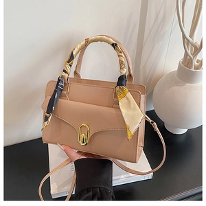 Detail of beige flap bag with gold twist lock and scarf-wrapped handle on books