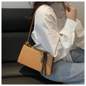 Detail of hand-woven straw shoulder bag with leather strap and decorative fringe tassel