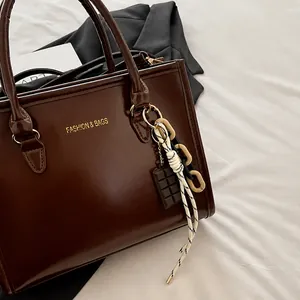 Detail of dark brown leather tote featuring a chocolate pendant and thick chain charms