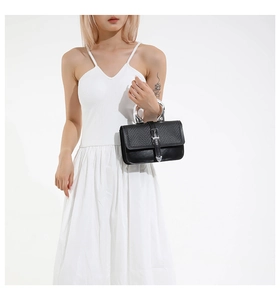 Detail of black leather handbag with silver U-shaped metal handle and heart buckle on model