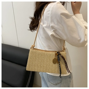 Detalle del bolso de hombro bohemio con dijes y textura de paja tejida elegante