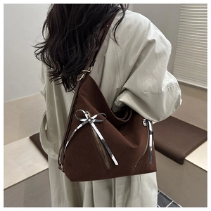 Detail of a brown canvas tote bag with decorative zippers and checkered ribbon bows