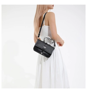 Detail view of black leather crossbody bag with silver sculptural metal handle on model