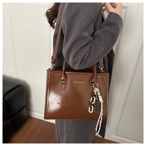 Brown faux leather tote bag with FASHION & BAGS logo and decorative ribbon charm