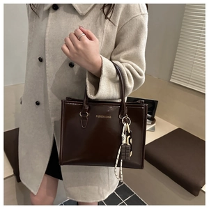 Detail of glossy brown tote bag with decorative knot charm worn with beige wool coat