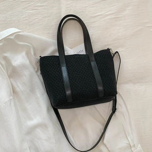 Detail of black woven bucket bag showing smooth leather handles and detachable shoulder strap