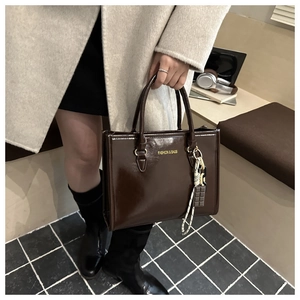 Detail of dark brown glossy tote bag with gold lettering and decorative bag charms