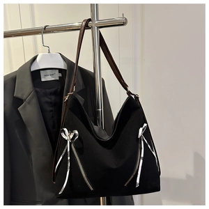Detail of black canvas tote bag with decorative zippers and silver bow charm accent