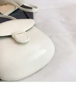 Close-up of minimalist cream white shell bag showing the matte leather texture and stitching