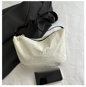 Detail view of cream nylon pleated crossbody bag showing texture and size comparison