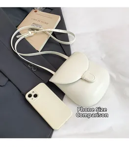 Detailed overhead view of cream leather crossbody bag next to phone for size scale
