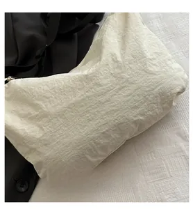 Detail of a cream-colored nylon crossbody bag with textured wrinkles and black strap