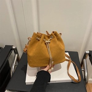 Caramel suede bucket bag with gold chain drawstring and pearl accents on white books