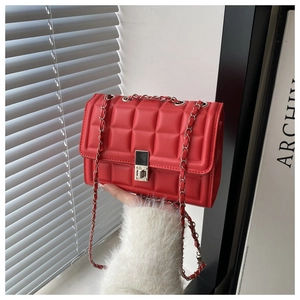 Detail of red quilted crossbody bag with metal chain strap and turn-lock closure