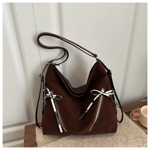 Detail of dark brown suede tote bag featuring diagonal silver zippers and striped bow ribbons